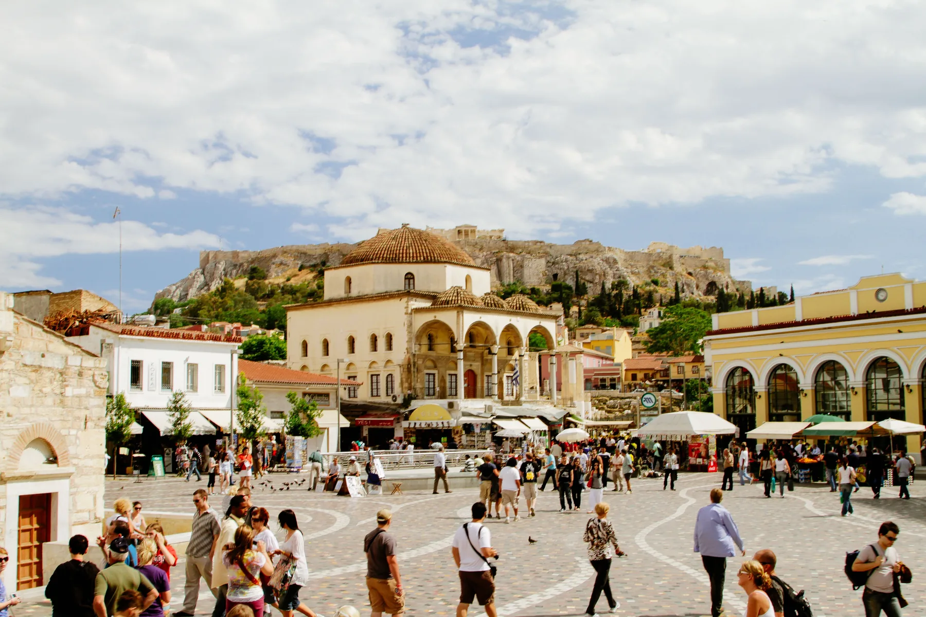 Monastiraki-pladsen i Athen i dagslys, med den kuppelformede gamle moské, butikker og Akropolis-klippen, der rejser sig bag tagene